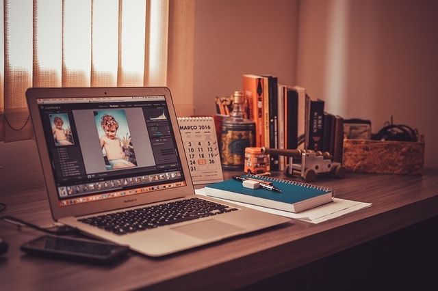 Laptop open on a wooden desk in a home office lit by warm evening light