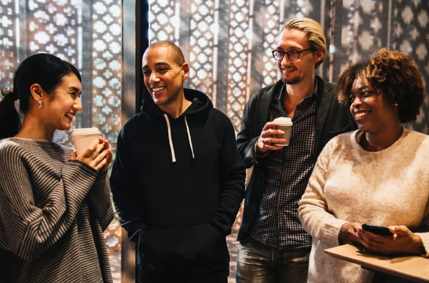 Four colleagues chatting with coffee cups in hand in an office
